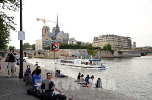 Người dân và du khách ngồi thư giãn bên bờ sông Seine, phía xa là Nhà thờ Đức Bà Paris. Ảnh: Hữu Chiến - PV TTXVN tại Pháp