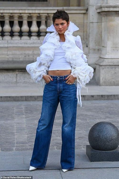 Zendaya cũng là một trong những gương mặt thu hút sự chú ý tại show. Nữ diễn viên 30 tuổi chọn phong cách trẻ trung hơn với quần jeans xanh, áo crop top và áo khoác trắng bèo nhún cầu kỳ, kết hợp giày mũi nhọn màu trắng cùng khuyên tai vòng vàng. Đây cũng là lần đầu Zendaya được bắt gặp tại Fashion Week trong mùa này. Cô xuất hiện cùng stylist Law Roach, thoải mái tạo dáng bên trong sự kiện và vẫy chào người hâm mộ khi đến địa điểm tổ chức. Ảnh: shutterstock, GC.
