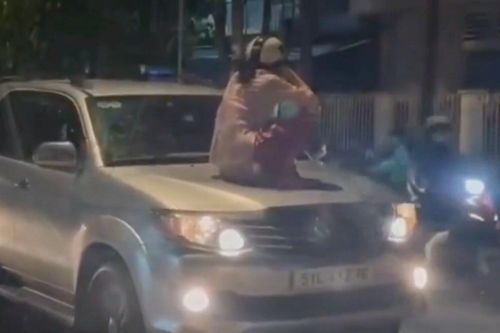Người phụ nữ ngồi trên nắp capo ô tô chạy trên đường ở Bình Dương