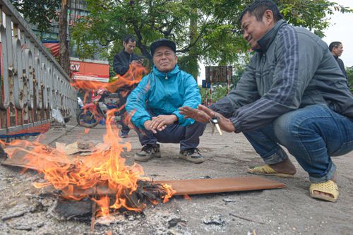 Người lao động đốt lửa sưởi ấm, mặc áo mưa tránh rét