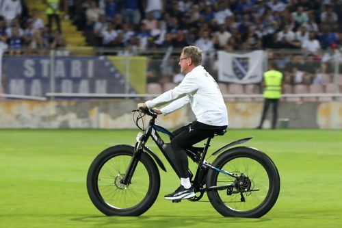 Cựu HLV Man United Ralf Rangnick đạp xe băng qua mặt sân cỏ
