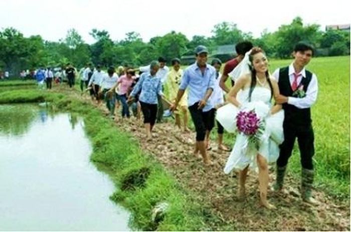 Cô dâu - chú rể cười hạnh phúc dìu nhau qua con đường lầy lội.