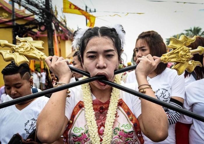 Theo quan niệm của các tín đồ Phật giáo, ăn chay là hành động cao cả thanh cao, còn những tập tục hành xác là để làm cơ thể, tâm hồn mình trong sạch hơn. Trong ảnh là một tín đồ đang thực hiện màn trình diễn của mình dưới sự giám sát của nhân viên y tế, người này đã xuyên thanh kim loại qua má bằng cách lắc mạnh đầu trước sự ngỡ ngàng của người xem. 