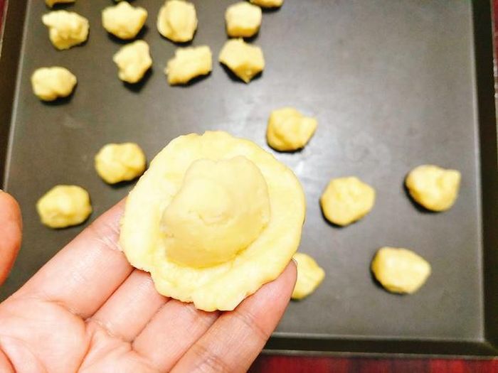 Ấn cho dẹt phần bột nước lại thành hình tròn sau đó lấy miếng bột dầu đặt vào giữa rồi túm lại cho kín. 