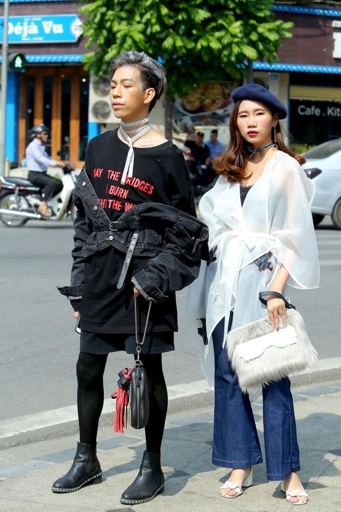 Cô gái bên cạnh tinh tế với set đồ gam màu trắng xanh, nhưng cậu bạn đi cùng lại lựa chọn những item thời trang khó hiểu. Chiếc túi xách tua rua, vòng choker cùng xu hướng diện áo khoác lệch vạt không phù hợp với hình ảnh mạnh mẽ của nam giới.