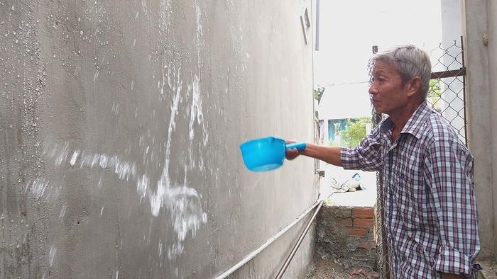 Tất cả nước đều trôi xuống khi ông Cách xối nước lên tường đã “sơn” chống thấm - Ảnh: Kim Hà.