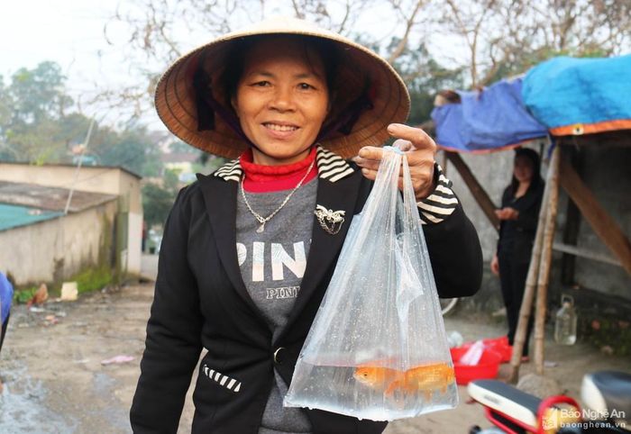 Một phụ nữ vui mừng vì đã chọn mua được 3 con cá chép vàng vừa ý để về cúng ông Táo.