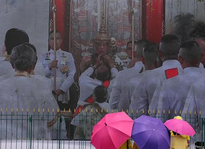Người dân quan sát vua Vajiralongkorn đeo vương miện qua một màn hình lớn. Thái Lan chấm dứt sự cai trị tuyệt đối của các vị vua vào năm 1932, nhưng nhà vua vẫn được tôn sùng, là biểu tượng và người bảo vệ của đất nước cũng như Phật giáo ở quốc gia này.