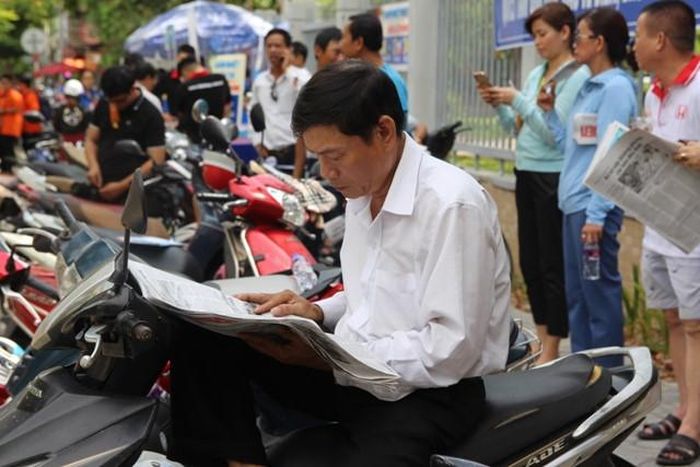 Tấp vội chiếc xe vào lề, một phụ huynh đọc báo trong lúc đợi con. 