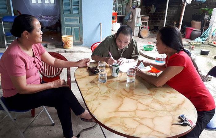 Bà Hà Bích Nhung, Phó Chủ tịch UBND xã Thanh Hưng và chị Nguyễn Thị Xuyến thăm và chi trả chế độ hàng tháng cho ông Ðàm Ngọc Quang, người bị nhiễm chất độc hóa học/dioxin. Ảnh: Mai Thủy