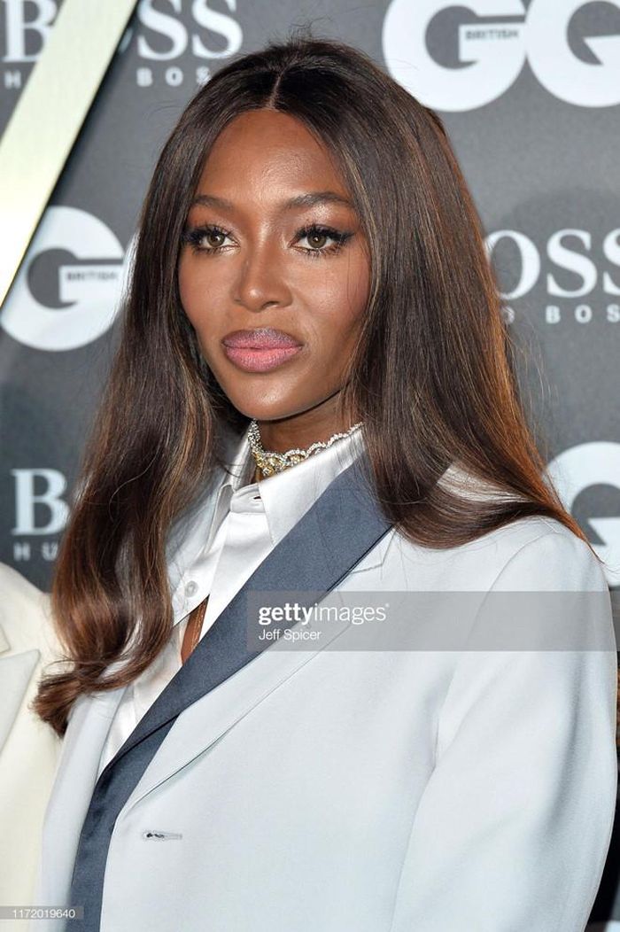Naomi Campbell phối sơ mi lụa với blazer dáng dài, quần ống đứng. Siêu mẫu lăng xê phong cách trang điểm tông màu gợi cảm.