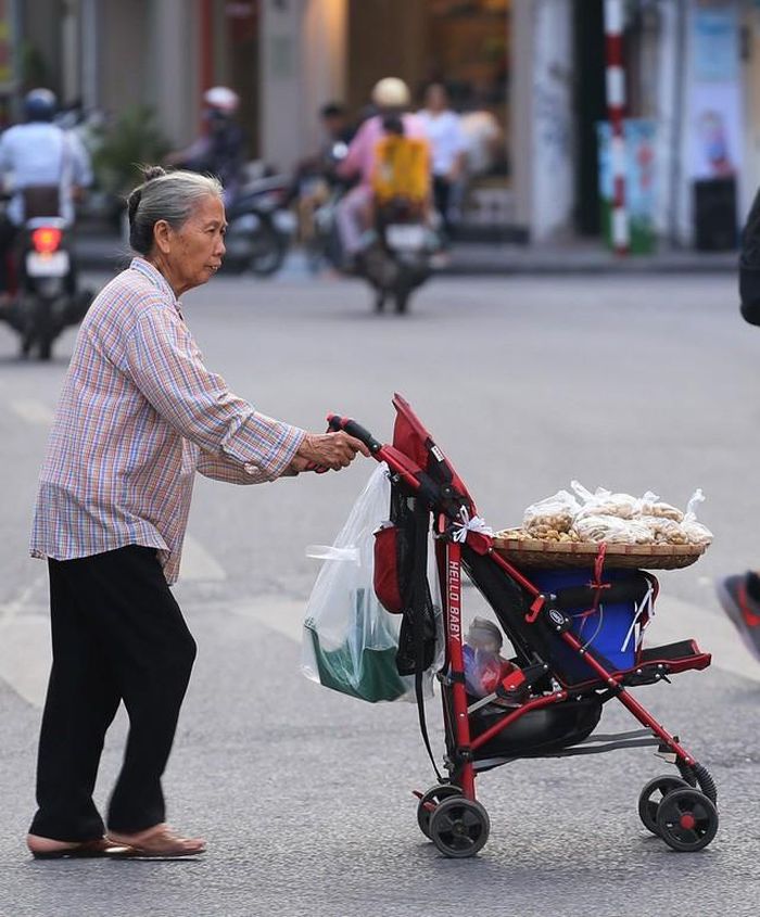 Người phụ nữ lớn tuổi đẩy chiếc xe bán hàng rong quanh những con phố cổ quen thuộc dưới tiết trời mát.