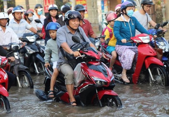 Phụ huynh chạy xe máy trên con đường ngập nước đưa con đến trường.