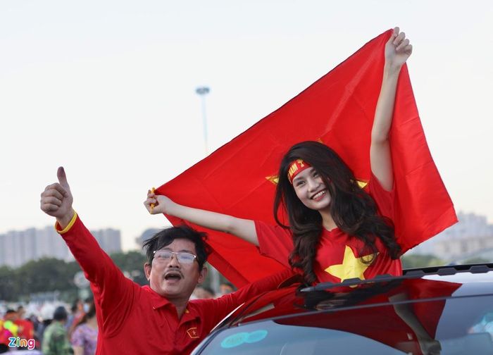  Nữ cổ động viên đứng trong ôtô, tay giương cao quốc kỳ Việt Nam và nở nụ cười rạng rỡ với niềm tin chiến thắng thuộc về thầy trò HLV Park Hang-seo. 