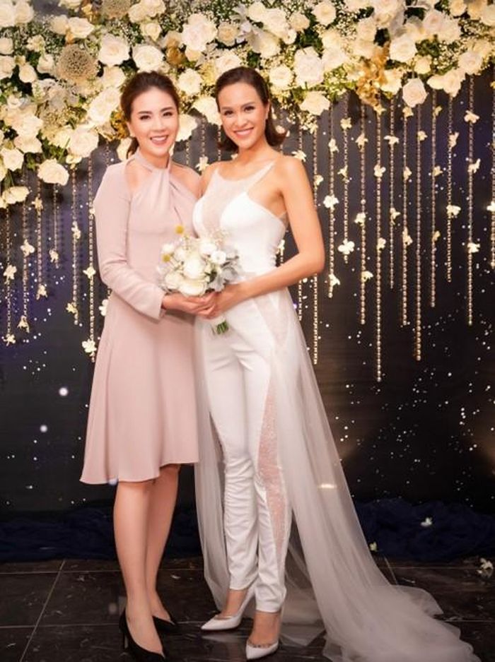 Phương Mai diện jumpsuit cưới cách điệu khi đón khách. Bộ trang phục được tô điểm bằng những đường cut-out, kết hợp satin thô và ren, điểm xuyết cườm. 