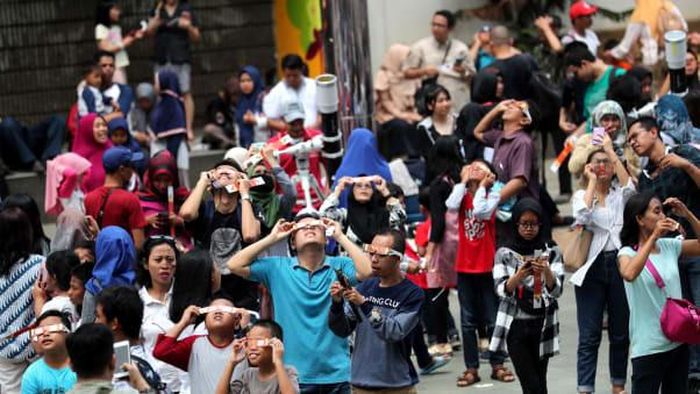 Một đám đông tụ họp ngoài trời ở thủ đô Jakarta, Indonesia, giơ kính bảo vệ để xem nhật thực