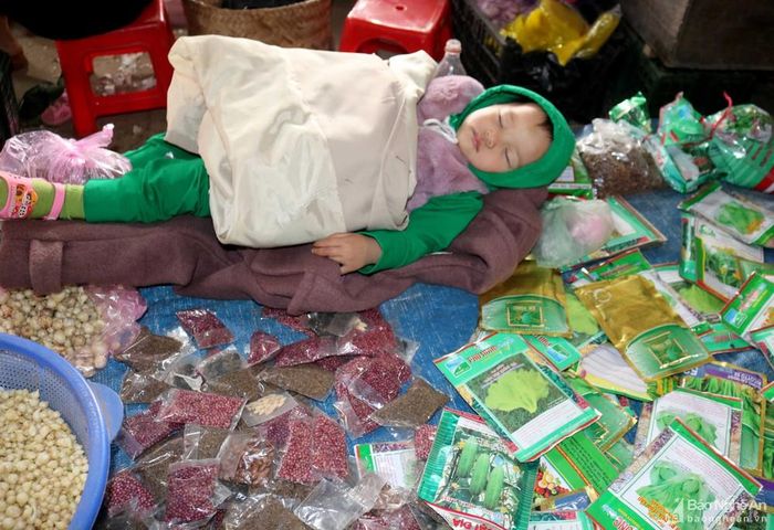 Những người dân buôn bán ở chợ quê phần lớn là nông dân. Hết mùa màng nông vụ họ lại ra chợ tần tảo "mua đằng ngược bán đằng xuôi" để mưu sinh. Không ít người đã phải mang cả con cái đi chợ, vừa trông con, vừa bán hàng. Trong ảnh: Mẹ bận bịu mua bán, một em bé ngủ ngon trên sạp hàng giữa chợ.