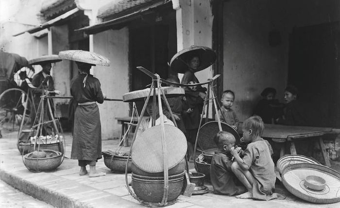  Người phụ nữ gồng gánh đi phía sau một chiếc xe kéo 