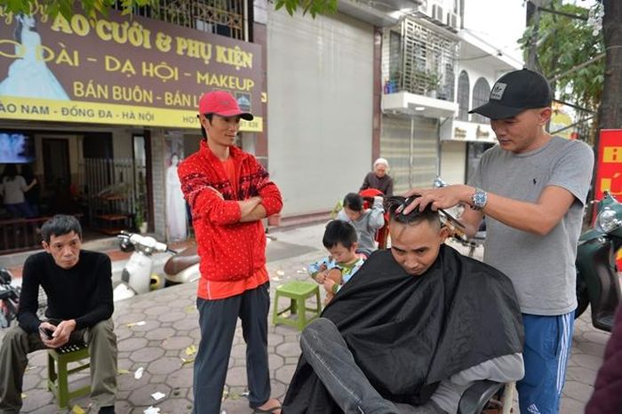 Các tiệm cắt tóc đông đúc là thế nhưng tại các quán cắt tóc vỉa hè cũng không dễ thở hơn là bao. Nhiều khách hàng vẫn phải chờ đợi từ 20 đến 40 phút để được cắt tóc. Hình ảnh được ghi lại trên phố Hào Nam, Hà Nội.