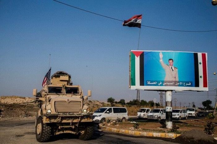 Xe quân sự Mỹ đi qua bảng hiệu có hình Tổng thống Syria Bashar al-Assad gần thành phố El-Kamyshli ở phía đông bắc Syria, hướng về phía các mỏ dầu ở tỉnh Deir ez-Zor, ngày 26/10/2019. (Ảnh: AP)