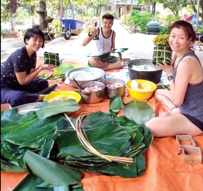Các bạn trẻ Singapore thích thú tham gia gói bánh chưng tại huyện Xuân Lộc, tỉnh Đồng Nai. Ảnh: LAN HƯƠNG