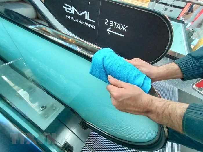 Làm vệ sinh diệt khuẩn trên tay vịn cầu thang cuốn trong trung tâm thương mại. (Ảnh: Trần Hiếu/TTXVN)