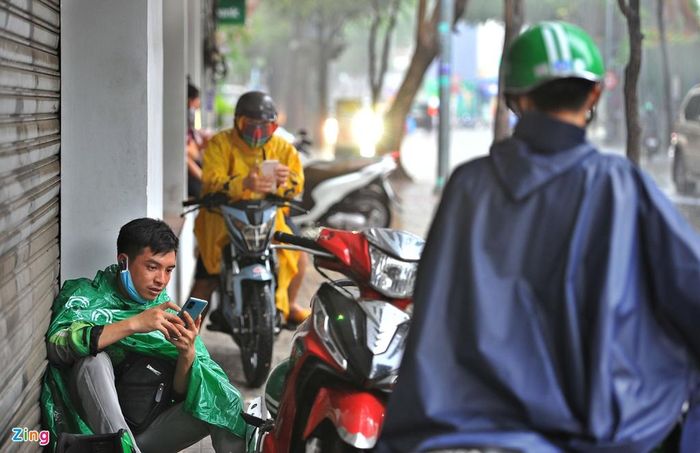 Quốc Phụng (tài xế xe Grab) trú mưa trên vỉa hè đường Nguyễn Thị Minh Khai. Người này cho biết cơn mưa bất chợt khiến nhiều khách hủy chuyến.