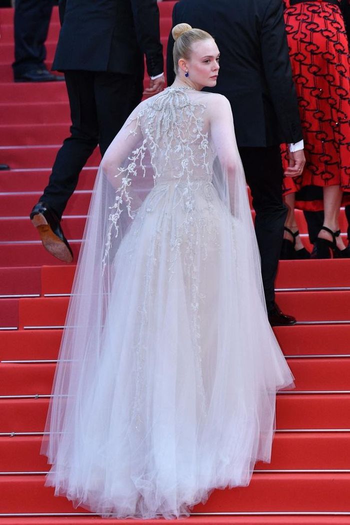 Tại thảm đỏ LHP Cannes, Elle Fanning là ngôi sao sáng với vẻ đẹp nữ tính, cổ điển. Cô từng xuất hiện cùng thiết kế váy trắng tinh khôi, khăn choàng trong suốt đính kết lấp lánh của Reem Acra.