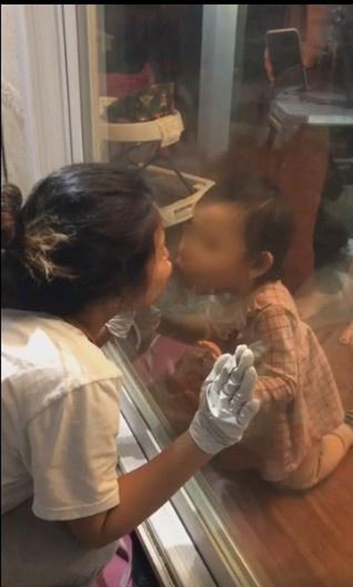 Trong video chia sẻ, Đình Bảo giả vờ đút cơm và chơi với con qua cửa kính, trong khi đó vợ anh thì hôn môi con qua lớp kính.
