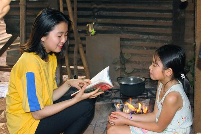 Em Lê Thị Hiếu (bìa trái) vừa nấu cơm vừa đọc sách cho em gái nghe. Ảnh: N.G