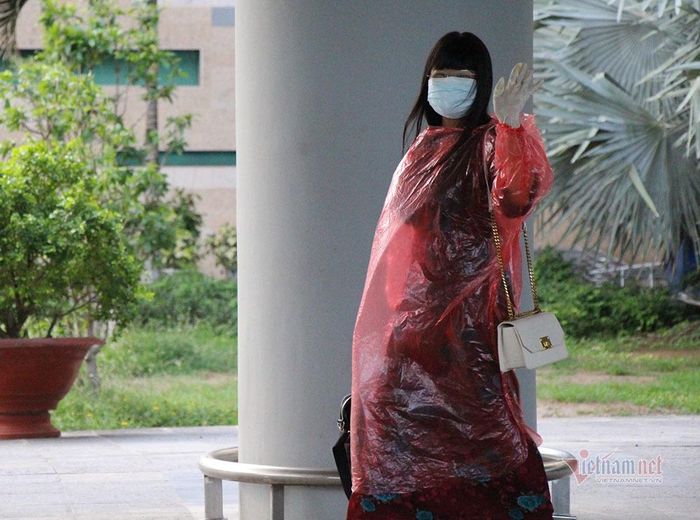 Một nữ du khách bảo hộ bằng áo mưa vẫy tay chào mọi người trước khi lên xe về khu cách ly 