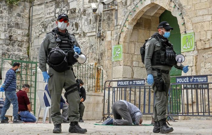  Tại giáo đường Al Aqsa ở Jerusalem, một thầy tế kêu gọi các tín đồ cầu nguyện Thượng đế "tha thứ cho chúng ta và toàn bộ nhân loại, cứu chúng ta khỏi đại dịch chết người này", theo AP. Trong ảnh, tín đồ Hồi giáo người Palestine quỳ cầu nguyện tại giáo đường Al Aqsa, bên cạnh binh sĩ Israel. Ảnh: AFP. 