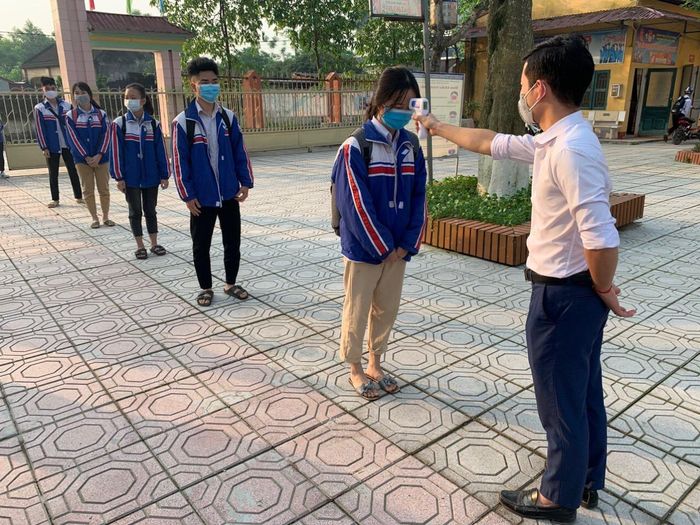 Nhân viên y tế kiểm tra thân nhiệt cho học sinh trước khi lên lớp.