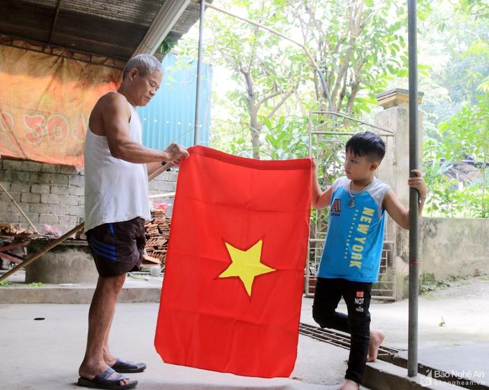 Ông Võ Đình Dân ở làng Nhùng, xã Tam Quang (Tương Dương) cùng cháu nội trân trọng treo lá cờ Tổ quốc trước nhà mình. Ảnh: Đình Tuân