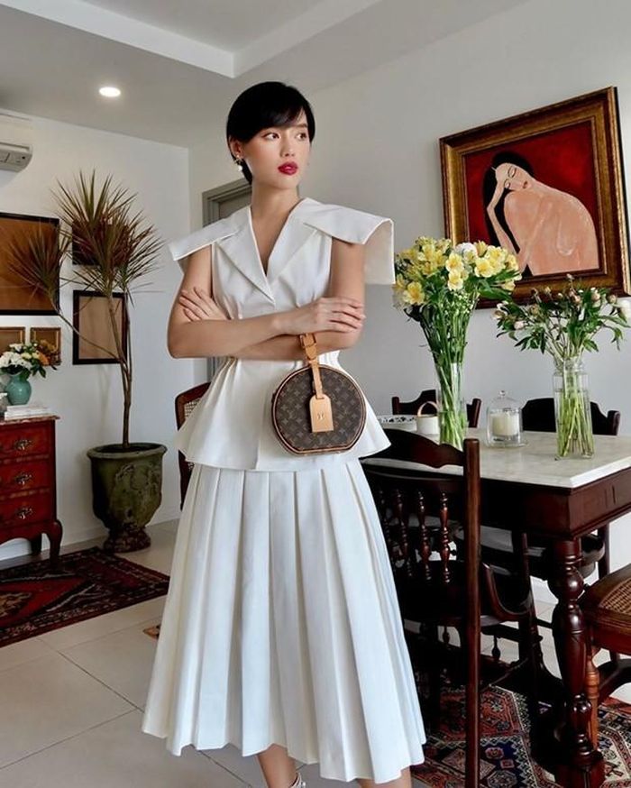 Ở nhà cũng phải đẹp là tôn chỉ của Khánh Linh. Với áo peplum và chân váy tiệp màu trắng, cô nàng chọn túi Boite Chapeau Souple của Louis Vuitton làm phụ kiện chấm phá, vừa thanh lịch vừa thời thượng.