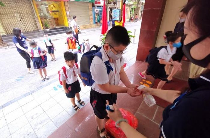 Học sinh trường Tiểu học Thăng Long (quận Hoàn Kiếm) thực hiện việc giãn cách và rửa tay sát khuẩn trước khi vào trường. Ảnh: TTXVN