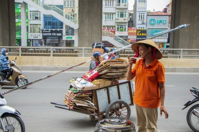 Dừng chiếc xe chở đầy giấy bìa, người lao động uống cốc nước với nụ cười tươi tắn trên môi. Ảnh: Việt Trinh.