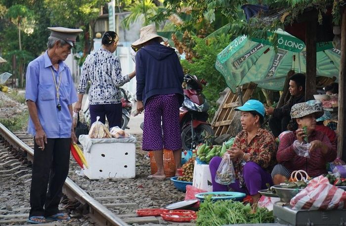 Nhân viên gác chắn tàu liên tục nhắc nhở người buôn bán di chuyển hàng hóa vào bên trong khi tàu đến gần