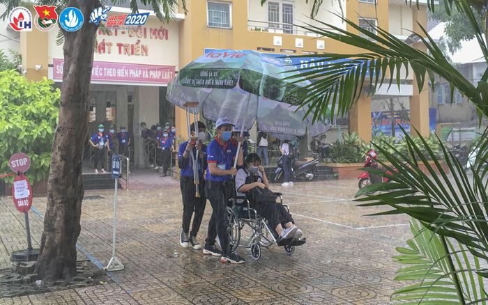 Một thí sinh nữ ngồi xe lăn được các bạn tình nguyện viên che dù khỏi ướt mưa tại Trung tâm Giáo dục thường xuyên quận Tân Bình (TPHCM)
