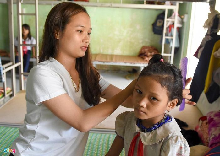  Cô giáo Đỗ Thị Bích Huyền, giáo viên trường Phổ thông Dân tộc bán trú Tiểu học &amp; THCS Sơn Bua, huyện Sơn Tây chăm sóc cho em Đinh Thị Pi, học sinh lớp 5A trước giờ đến lớp. "Do nhà ở quá xa, các em học sinh làng Nước Mù phải ở lại bán trú của trường để học tập. Ngoài giờ dạy học trên lớp, chúng tôi còn dạy kèm, chăm sóc các em ở khu bán trú", cô giáo Huyền chia sẻ. 