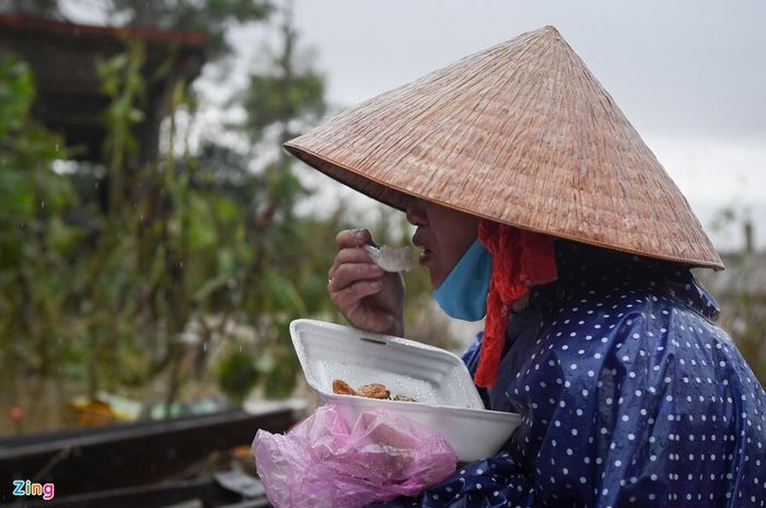  Trong những ngày đầu, bếp bị ngập nước. Người dân chủ yếu ăn mì tôm sống. Dần dần, những đoàn cứu trợ đến giúp người dân có cơm ăn. Trong ảnh, một người dân xóm Cồn tranh thủ ăn hộp cơm cứu trợ ngay trên thuyền trong cơn mưa. 