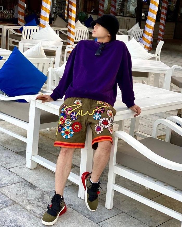Karik mặc áo sweater màu tím đậm kèm quần shorts in họa tiết hoa mặt cười. Anh chọn thêm sneakers phối màu giống trang phục và phụ kiện mũ, kính mắt. Ảnh: @karik.koniz.