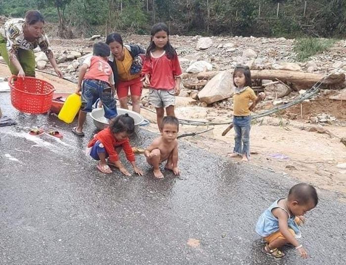 Những đứa trẻ phong phanh trong bộ quần áo cũ, trong khi người thân đang giặt giũ quần áo trên đoạn đường còn sót lại sau lũ. 