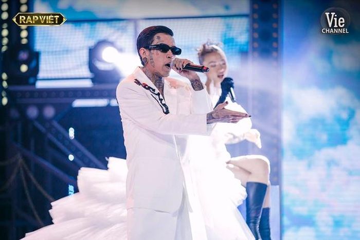  Tại Rap Việt, Dế Choắt gây ấn tượng khi đầu tư kỹ lưỡng cho từng màn trình diễn. Bên cạnh phong cách độc đáo, trang phục giúp nam rapper cũng thu hút khán giả. Trong đêm chung kết, anh diện bộ suit trắng độc đáo với phần tà hai lớp cùng dòng chữ "Dế Choắt" thêu trên cầu vai và "strawberry" (dâu tây) ở phần lưng nhằm ngụ ý về bài hát thể hiện cùng huấn luyện viên Wowy. Ảnh: Rap Việt. 