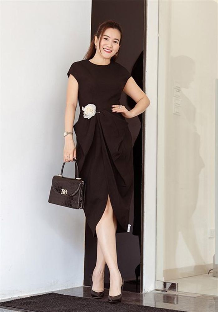 Doanh nhân Anh Thơ thanh lịch với bộ đầm tạo phom bằng những đường xếp nếp khéo léo, mang dấu ấn đặc trưng của Đỗ Mạnh Cường. Hoa cài màu trắng tương phản trở thành điểm nhấn trên nền trang phục và phụ kiện đen.