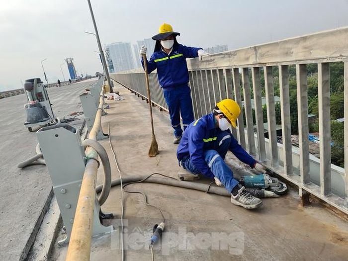 Trong khi một nhóm công nhân khác thi công đánh sạch bản thép mặt cầu ở lề đi bộ trước khi thi công lớp bê tông nhựa trên bề mặt.