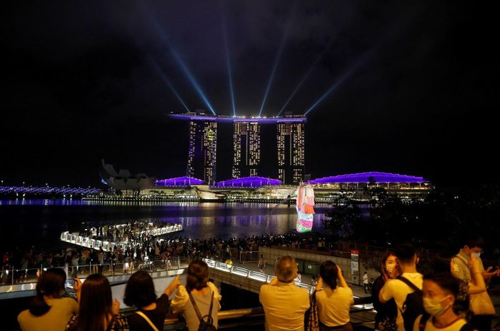  Người dân Singapore theo dõi màn trình diễn ảnh sáng tại vịnh Marina. Năm nay, Singapore hủy bỏ bắn pháo hoa do đại dịch Covid-19. Ảnh: Reuters. 