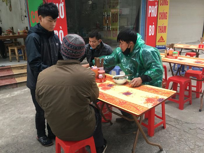 Một người đàn ông phải mặc nguyên bộ áo tơi khi ăn phở trên đường Lê Trọng Tấn (Hà Đông - Hà Nội) sáng nay 8-1 vì trời rét buốt. Ảnh: VĂN PHÚC