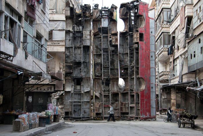  Tại Aleppo, ngày 14/3/2015, một cậu bé đi cạnh rào chắn làm bằng ba chiếc xe buýt hỏng, được dựng lên để cản tầm nhìn của lính bắn tỉa từ quân đội Tổng thống Assad. Ảnh: AFP. 