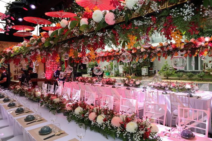 Bánh sinh nhật 2 tầng với nhiều chi tiết theo phong cách cổ trang. Không gian bữa tiệc ấm cúng với đèn lồng, ô màu đỏ.